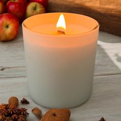 a lit candle sitting on top of a wooden table next to an apple and cinnamon