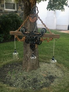 a wooden cross hanging from a tree in front of a house with two bells attached to it