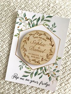 save the date magnets on top of a card with greenery and leaves around them