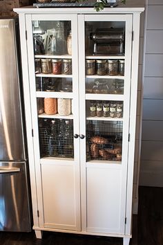 a white cabinet with glass doors next to a refrigerator