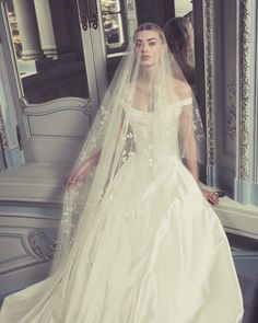 a woman in a white wedding dress standing next to a mirror wearing a long veil