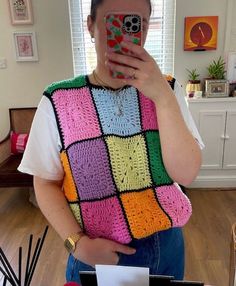 a woman taking a selfie while wearing a colorful crocheted vest and holding a cell phone