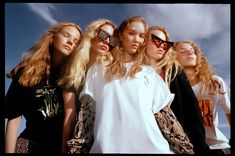 four women standing next to each other in front of the ocean with their sunglasses on