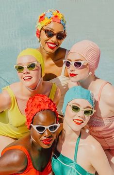 four women in bathing suits and sun glasses posing for the camera