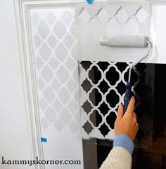 a person painting a wall with white and black tiles on it's side, next to a fireplace