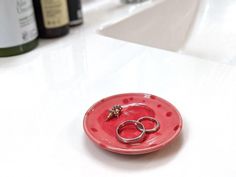 two wedding rings on a red plate with wine bottles in the background