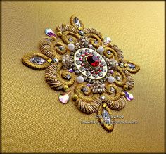 a gold brooch with red and white stones on it's center, sitting on a yellow cloth