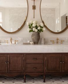 two round mirrors are above the double sink vanity in this bathroom with marble countertops and wood cabinetry