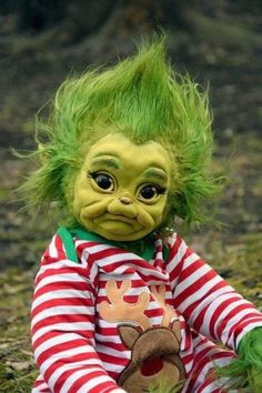 a troll doll with green hair sitting on the ground wearing a red and white striped shirt