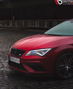 a red car is parked on the cobblestone road