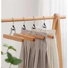 two wooden clothes hangers with pants hanging from them on a wood rail in front of a window