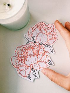 a person's hand is pointing at a sticker with flowers on it next to a jar of yogurt