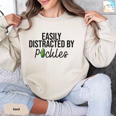 Stay cozy and showcase your quirky side with our "Easily Distracted by Pickles" sweatshirt. Featuring a fun pickle graphic, this soft and comfortable sweatshirt is perfect for casual wear or lounging at home. Embrace your love for pickles and add a touch of humor to your wardrobe. --- How To Order ----- 1-) Please, check and review all the photos. 2-) Choose your sweatshirt size and color. 3-) Click add to cart. You can go back to add more sweatshirts. 4-)Click "Proceed to check out". 5-)When yo Funny Crew Neck Sweatshirt With Relaxed Fit, Funny Relaxed Fit Crew Neck Sweatshirt, Funny Slogan Sweatshirt In Relaxed Fit, Relaxed Fit Crew Neck Sweatshirt With Funny Text, Funny Text Relaxed Fit Sweatshirt, Cute Slogan Sweatshirt Relaxed Fit, Relaxed Fit Sweatshirt With Funny Print For Loungewear, Pickle Graphic, Pickles Sweatshirt