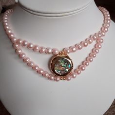 This lovely pearl and abelone necklace is made with 7x9mm pink pearls and a 20mm abelone coin, which has abelone on both sides. A beautiful gift for any occasion. Elegant Gold Abalone Shell Jewelry, Elegant Gold Jewelry With Abalone Shell, Gift Jewelry With Abalone Shell Round Beads, Gift Round Beads Jewelry In Abalone Shell, Elegant Pink Mother Of Pearl Necklace, Elegant Abalone Shell Necklace As Gift, Pearl Jewelry With Mother Of Pearl Buttons For Gift, Elegant Abalone Shell Necklace For Gift, Elegant Gold Necklace With Abalone Shell