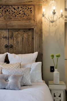 a bed with white sheets and pillows in front of a wooden headboard that has a chandelier above it