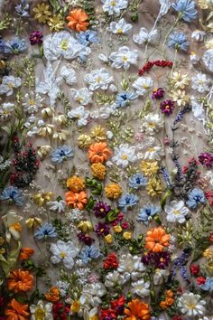 an assortment of colorful flowers are arranged on a tablecloth with white, orange, and blue flowers