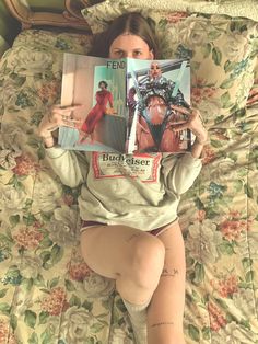 a woman laying in bed with her legs crossed and reading a magazine on top of her