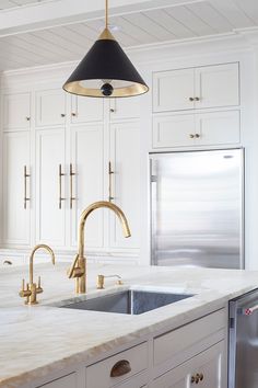 a kitchen with marble counter tops and gold faucet lights over the sink, along with white cabinets