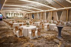 a banquet hall with tables and chairs covered in white tablecloths, gold sashes and bows