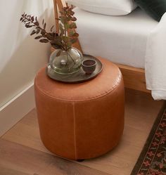 a small round stool with a plant in it on the floor next to a bed