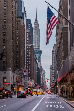 an empty city street with tall buildings and cars driving down the road in front of it