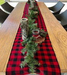 a long table is decorated with red and black buffalo checkered runneres, pine cones, mason jars and evergreen branches