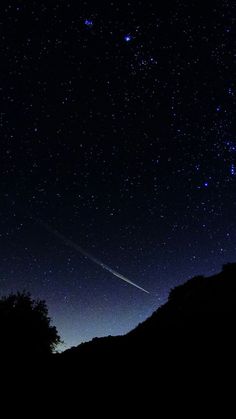 the night sky is filled with stars and some trees in front of a dark hill