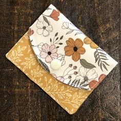 a yellow and white flowered napkin with a button on the front sitting on a wooden surface