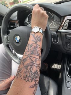 a person driving a car with a tattoo on their arm and wrist, holding the steering wheel