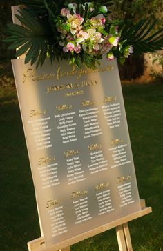 a sign with flowers and greenery on it sitting in the grass near some trees