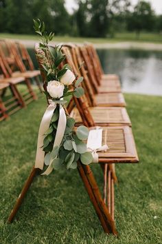 a row of wooden chairs with flowers and greenery tied to them on the grass