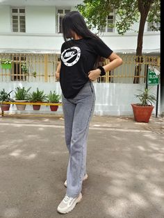 a woman standing in the street with her back turned to the camera, wearing jeans and a black t - shirt