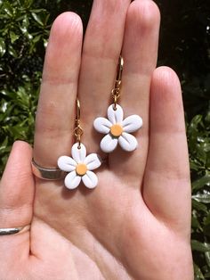 a hand holding two white and yellow flower earrings