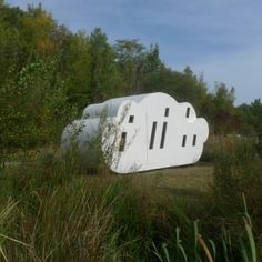 a large white object sitting in the middle of a forest filled with tall grass and trees