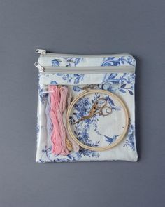 a pair of scissors and some thread in a bag on a gray background with blue flowers