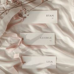 three place cards are laying on a bed with pink sheets and flowers in the background