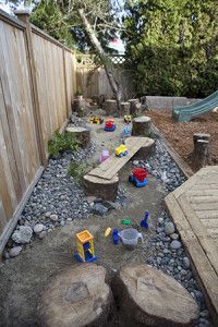 an outdoor play area with rocks, sand and water toys in the back yard next to a wooden fence