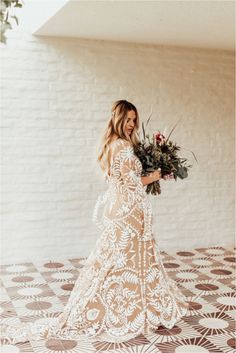 a woman in a white lace dress holding a bouquet of flowers and looking at the camera