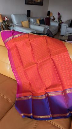 The saree is a Ganga jamuna saree with different coloured borders . It is an orange coloured saree with gold checks in the body . The pallu is purple colour . Orange Handloom Pre-draped Saree For Puja, Orange Banarasi Silk Handloom Saree, Orange Katan Silk Saree For Puja, Orange Tussar Silk Dupatta For Puja, Orange Paithani Silk Saree For Diwali, Orange Handloom Tussar Silk Saree, Orange Paithani Silk Saree With Pallu, Orange Paithani Silk Saree For Festivals, Orange Handloom Katan Silk Dupatta