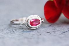 a close up of a ring with a red stone on it and a flower in the background