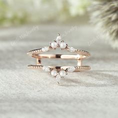 two rings with pearls on them sitting in front of a pine tree and snow covered ground