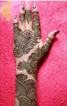 a woman's hand with henna tattoos on it and pink wall in the background