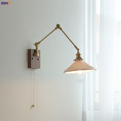 a wall mounted lamp on the side of a white wall next to a curtained window