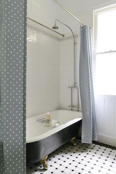 a bath tub sitting under a window next to a shower curtain in a bathroom with black and white tiles