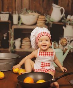 a baby in a chef's outfit sitting on the floor next to some oranges