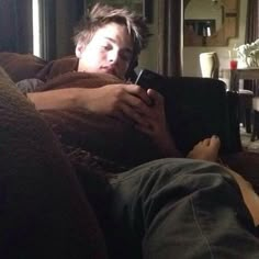 a young man laying on top of a couch holding a cell phone in his hand