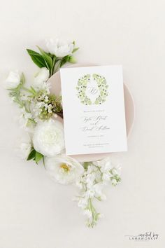 the wedding stationery is surrounded by white flowers and greenery on a pink plate