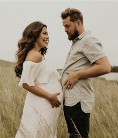 a pregnant woman standing next to a man in a field with tall grass on the ground