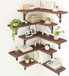 three wooden shelves with books, plants and pictures on them are arranged in a corner