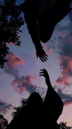 two hands reaching for each other in front of a sky with clouds and trees at night